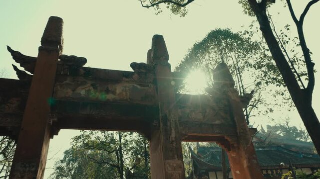 Weathered stone ceremonial gate framed by trees in Chongqing, China