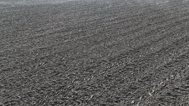 Freshly ploughed dark soil clods and furrows with crop residue in close detail revealing a greenhouse on the winter horizon, Po Valley, Italy, low drone forward glide with tilt up reveal