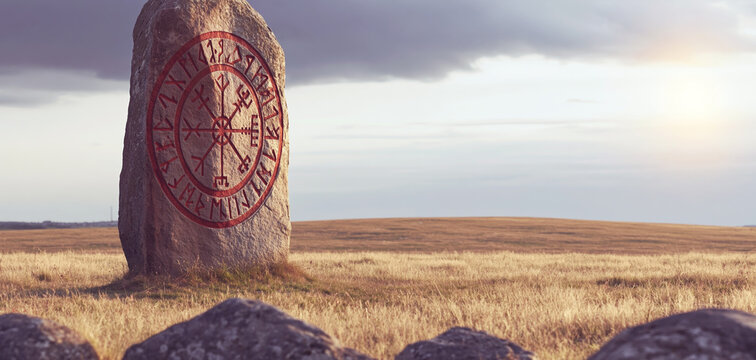 Ancient Norse runestone with red Vegvisir compass symbols standing in a windswept golden field beneath a dramatic evening sky