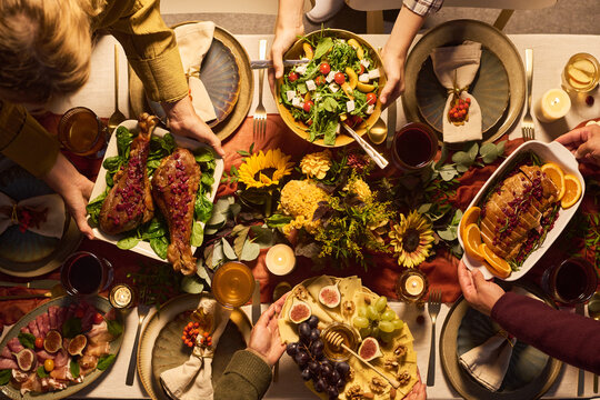 Top view of adults sharing festive autumn dinner dishes at decorated table. Concept represents holiday gathering, ideal for Thanksgiving catering marketing