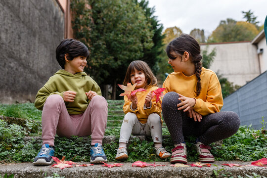 Three Smiling Children Playing with Colorful Autumn Leaves on a Garden Step
