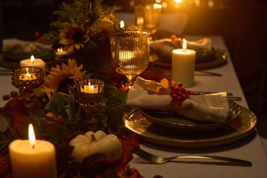 Festive Thanksgiving dinner table setting featuring burning candles, pumpkin, floral arrangements and tableware. Suitable for autumn holiday catering, event planning and restaurant promotion