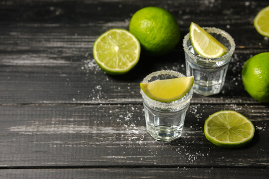 Tequila shots with lime wedges and thyme on a dark wooden background
