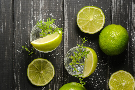 Tequila drink with fresh thyme and lime slices on dark wood background