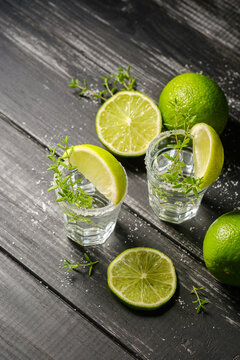 Tequila with fresh thyme and lime slices on a dark wooden background