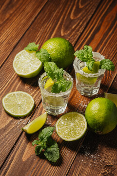 Tequila shots with lime and mint garnishes on a wooden table