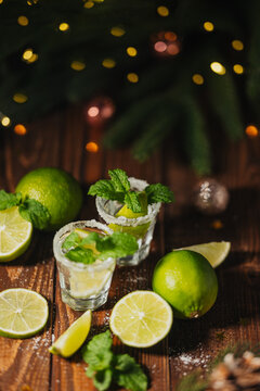 Tequila cocktails with lime and mint on wooden table with festive lights