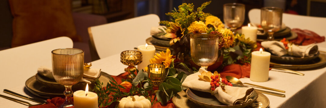 Table setting featuring festive autumn dinner decoration with lit candles, glassware, and flowers representing celebration. Visual ideal for Thanksgiving dinner marketing and catering campaigns