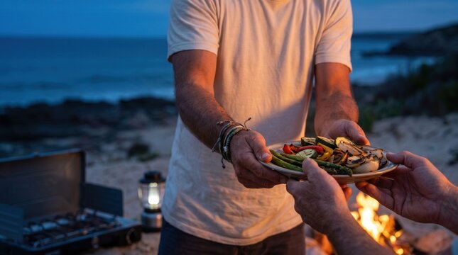Hands passing a plate of food beside a coastal campfire