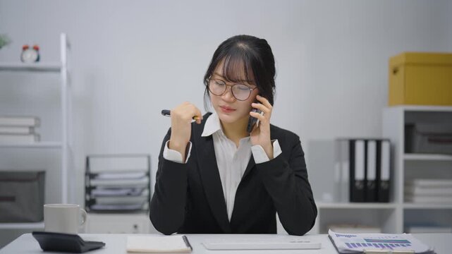 Young professional woman in black suit talking on the phone while working with paperwork in modern office setting