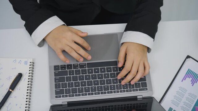Business person typing on laptop keyboard with notebook and smartphone on white desk in office environment