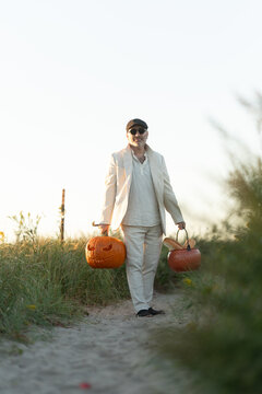 Man carrying two pumpkins along a sandy path through coastal grass. A man carries two pumpkins on a sandy path through grass at a coastal location in daylight.