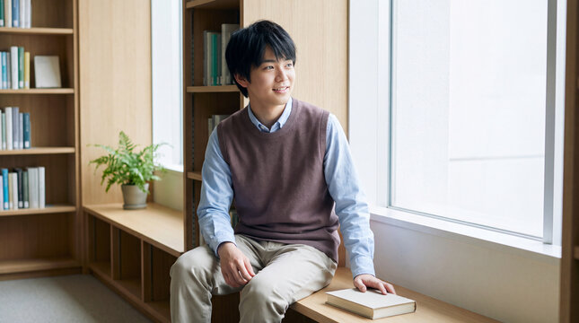 図書館のベンチで本を手に穏やかに微笑む二十代男性 | ナチュラル
