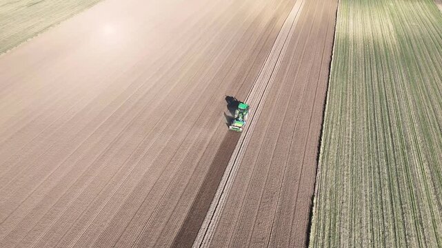 Aerial view of tractor plowing and sowing seeds in a large agricultural field, showcasing the continuous action of farming across the landscape with visible furrows and soil