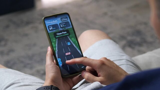 Person plays a fast-paced mobile driving game, steering a virtual car through city traffic and road barriers while reacting to changing speed and obstacles.