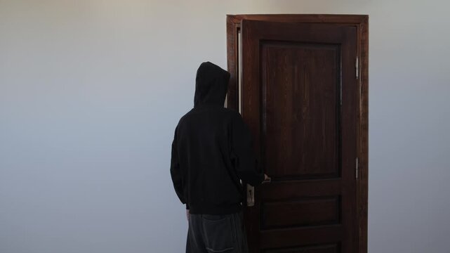 Anxious man talking to himself before leaving home, struggling with hesitation and self doubt, repeatedly opening and closing the door, pacing indoors and avoiding going outside, emotional distress