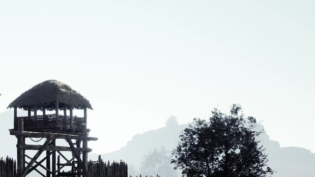 In a serene landscape, ancient wooden watchtowers rise against a misty sky. Silhouetted mountains provide a breathtaking backdrop, creating a sense of timelessness and calm.