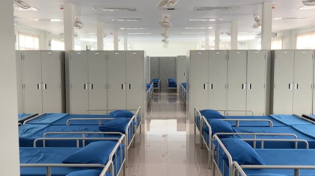 Interior shot of a clean and organized military barracks room with rows of blue beds and white lockers.