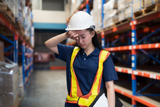 Warehouse workers, warehouse storage and logistics. Asian warehouse female worker headache, stressed feeling while working in storage warehouse