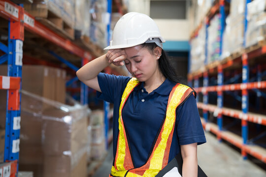 Warehouse workers, warehouse storage and logistics. Asian warehouse female worker headache, stressed feeling while working in storage warehouse