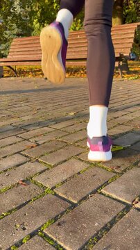 Close-up rear view of a woman jogging in place and doing high knees in an autumn park. Sports training, warm-up routines, and healthy lifestyle concepts