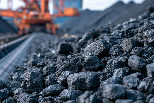 Raw coal rocks transported on industrial conveyor belt with mining machinery in background. Energy production concept for heavy industry ads.
