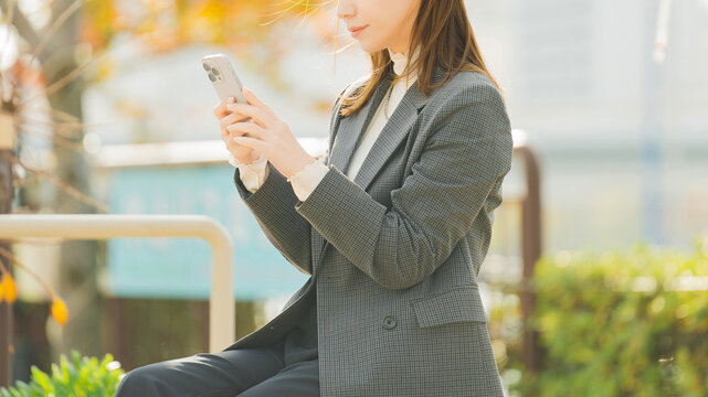 紅葉の街路樹とスマートフォンを使う女性・ビジネスウーマン