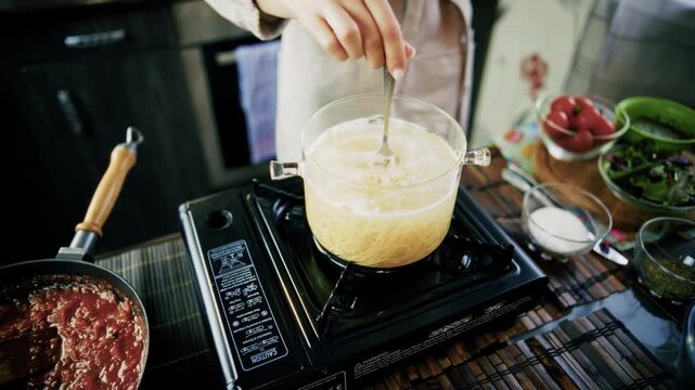 Stirring Boiling Pasta In Glass Pot Beside Pan With Red Sauce 