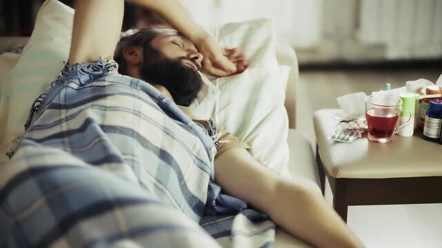 Sick Man Lying On Sofa With Thermometer Feeling Unwell. Cold And Flu Illness 