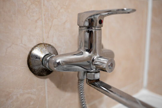 Old bathroom faucet with limescale and rust on beige tile wall copy space