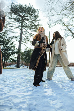 Women throw a snowball with friends in a winter park