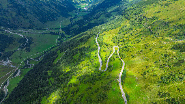 Aerial view of a winding mountain road through the lush green valley of the Austrian Alps, featuring dramatic switchbacks and scenic landscapes
