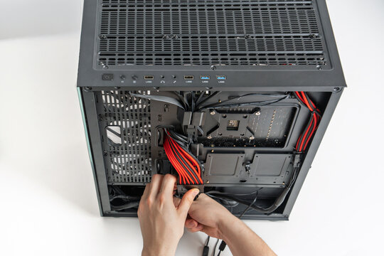 Technician assembling desktop computer hardware, connecting power cables to motherboard inside black PC case, isolated on white background studio shot