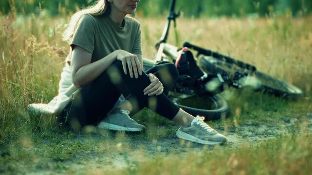 Woman Resting On Grass Beside Bicycle While Suffering From Leg Injury 