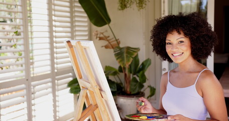 Painting on canvas, woman smiling and holding paintbrush in bright room © WavebreakMediaMicro