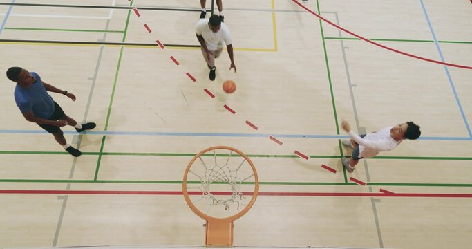 Diverse male friends dribbling basketball, playing offense, laying up, dunking and scoring on court