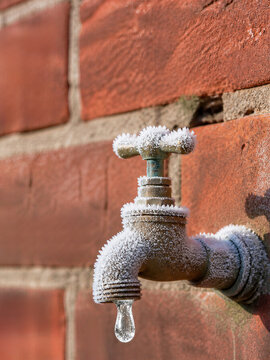 Frozen outdoor faucet with hanging ice drop on weathered brick wall