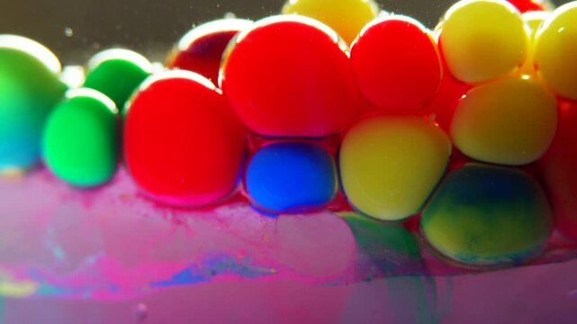 Macro of red, yellow and green watercolor paint spheres in oil, a blue streak slowly bleeding inside one droplet. Side view, shallow depth of field, real time 4K.