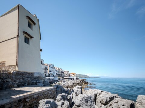 Cefal&ugrave;, Sicily, Italy. An impressive tall coastal house built into jagged limestone rocks overlooking the blue sea.