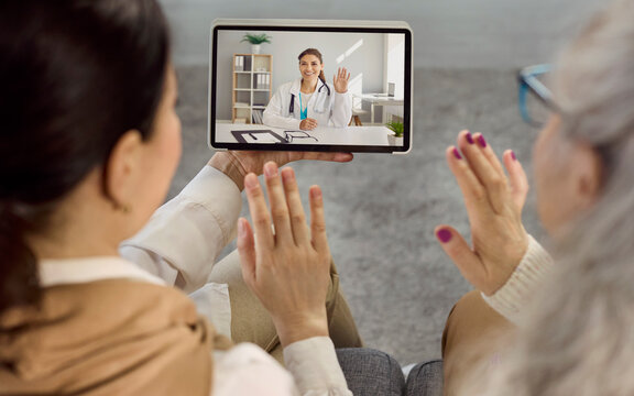 Doctor patient senior caregiver tablet online video consultation. Cheerful telemedicine call shows a doctor waving enabling remote advice. Concept highlights trusted virtual healthcare access.