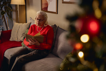 Fototapeta na wymiar Senior Caucasian woman reading book alone at Christmas time. Image suitable for senior mental health campaigns, retirement lifestyle marketing and holiday solitude awareness