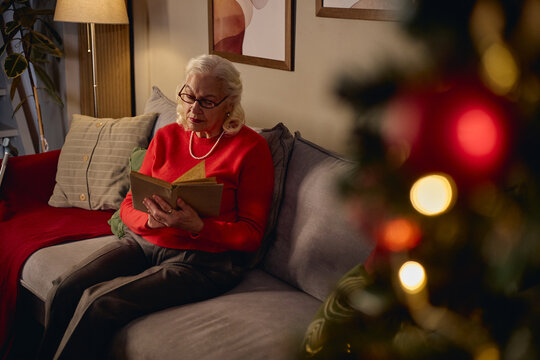 Senior Caucasian woman reading book alone at Christmas time. Image suitable for senior mental health campaigns, retirement lifestyle marketing and holiday solitude awareness