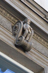 A low angle view of an ornate historic building facade featuring a decorative cherub statue holding a tablet on a stone corbel. © nahhan