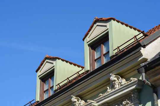 Low angle view of a classic architectural building facade featuring two traditional green dormer windows with orange roof tiles under a clear blue sky.