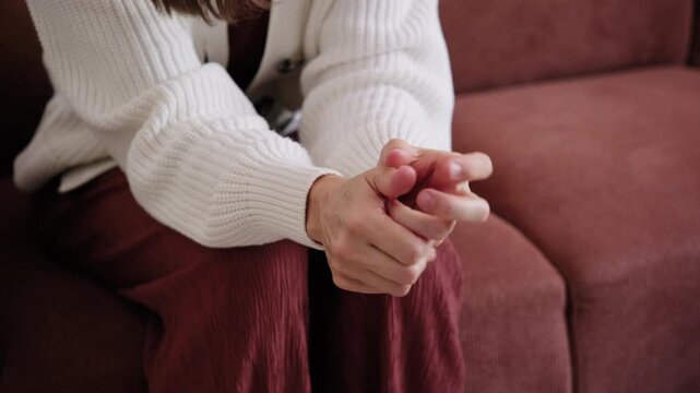 Close-up of an anxious woman wringing her hands and fidgeting nervously while sitting on a sofa indoors.
