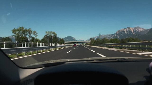 View from car interior driving along A23 highway towards Tolmezzo under clear blue summer sky.