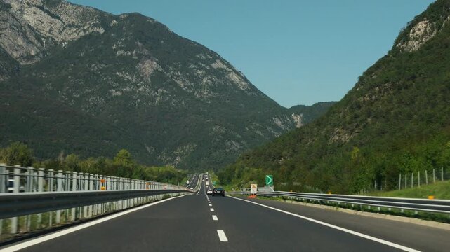 Automobile driving along asphalt highway through alpine valley surrounded by steep mountain peaks.
