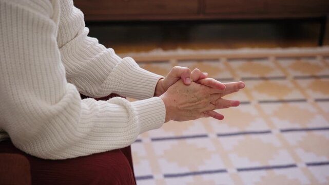 Close-up of a woman sitting indoors with trembling hands, fidgeting and rubbing fingers due to severe nervous tension, stress, and anxiety.