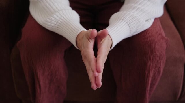 Close-up of a woman rubbing her hands and fidgeting nervously while sitting on a couch, showing signs of anxiety, stress, or impatience.