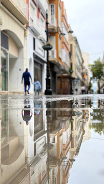 Rain soaked city street reflecting historic architecture and pedestrians walking through a quiet urban neighborhood